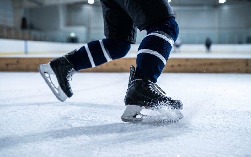hockey player mid-stride with ice spraying off the planted skate, showing how a locked-in fit transfers power to the blade edges