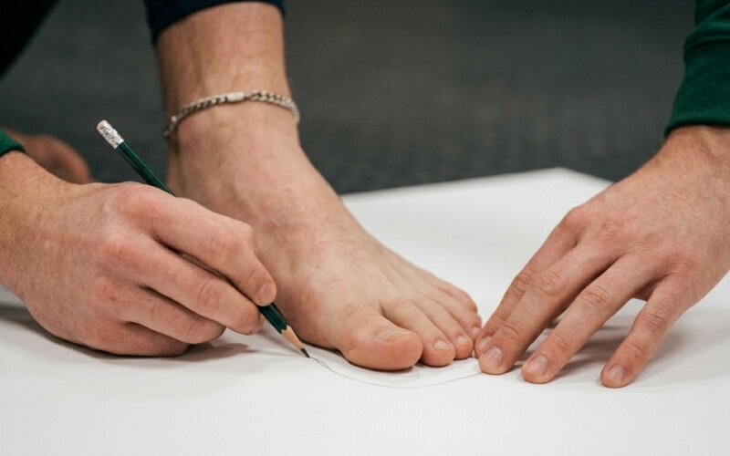 person tracing a bare foot outline on white paper with a pencil to measure foot length and width for hockey skates